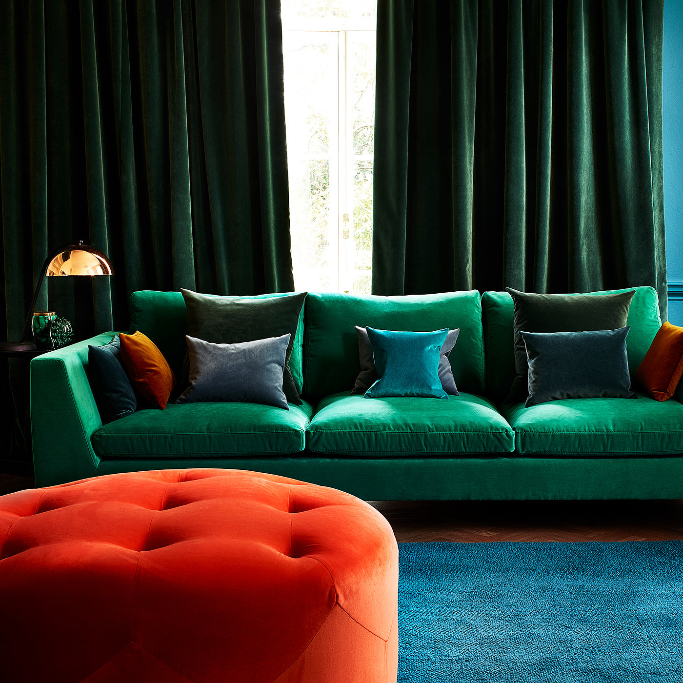 Sofa covered in green velvet upholstery fabric and footstall in orange velvet upholstery fabric